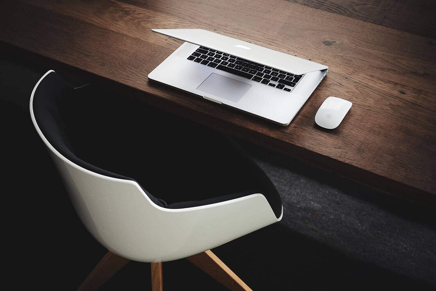 Downward view of a skinny wooden desk with a half closed Apple laptop on it